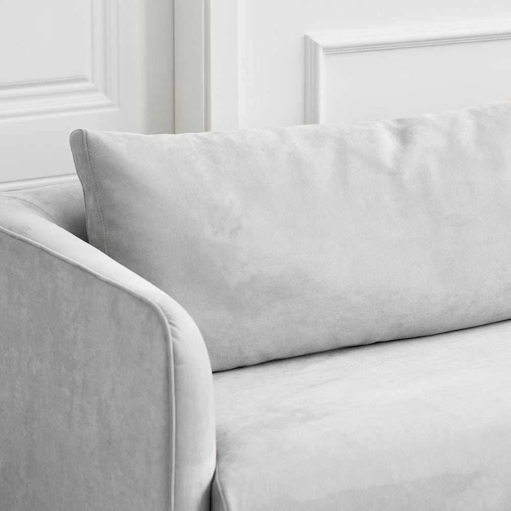 A close-up of a light gray upholstered sofa with a large rectangular back cushion and part of the arm visible, set against a white paneled wall.