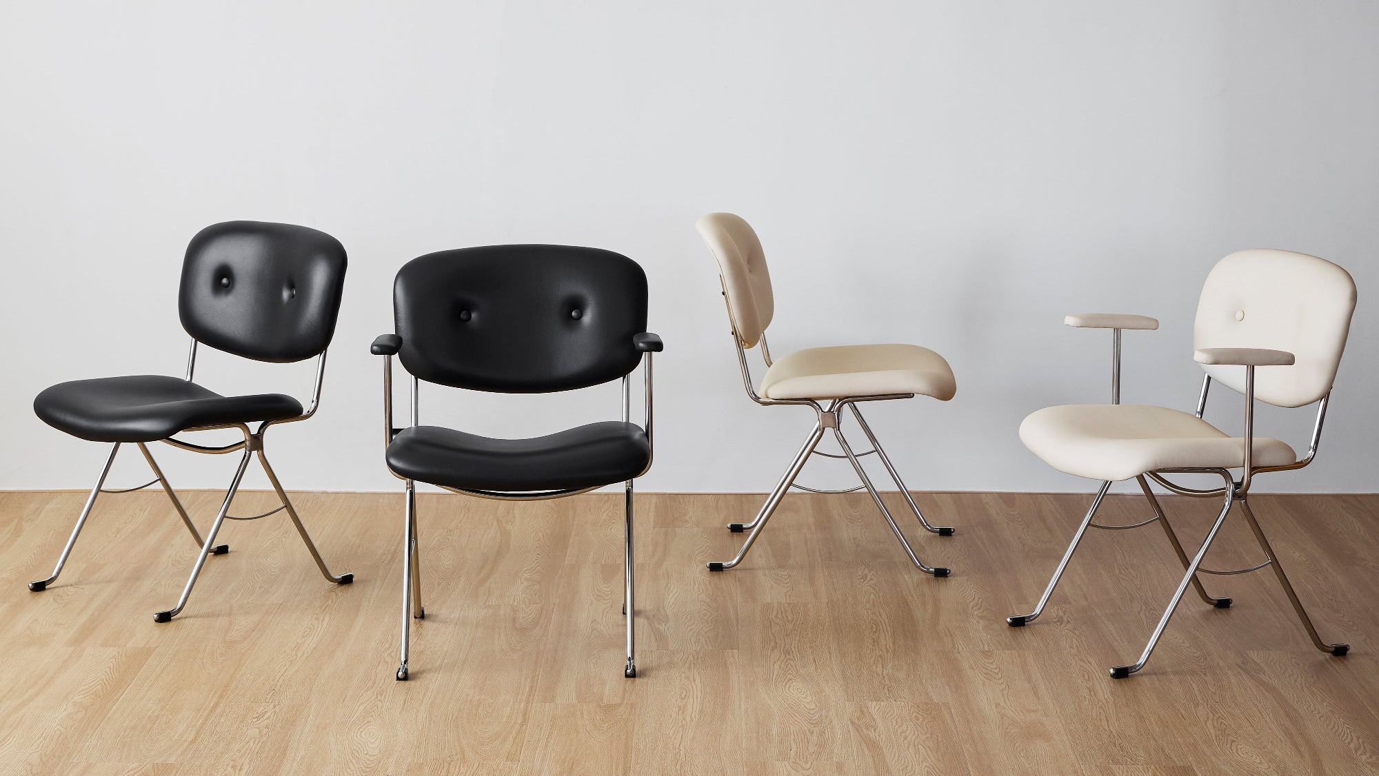 Four chairs in black and beige on a wooden floor with a white wall background