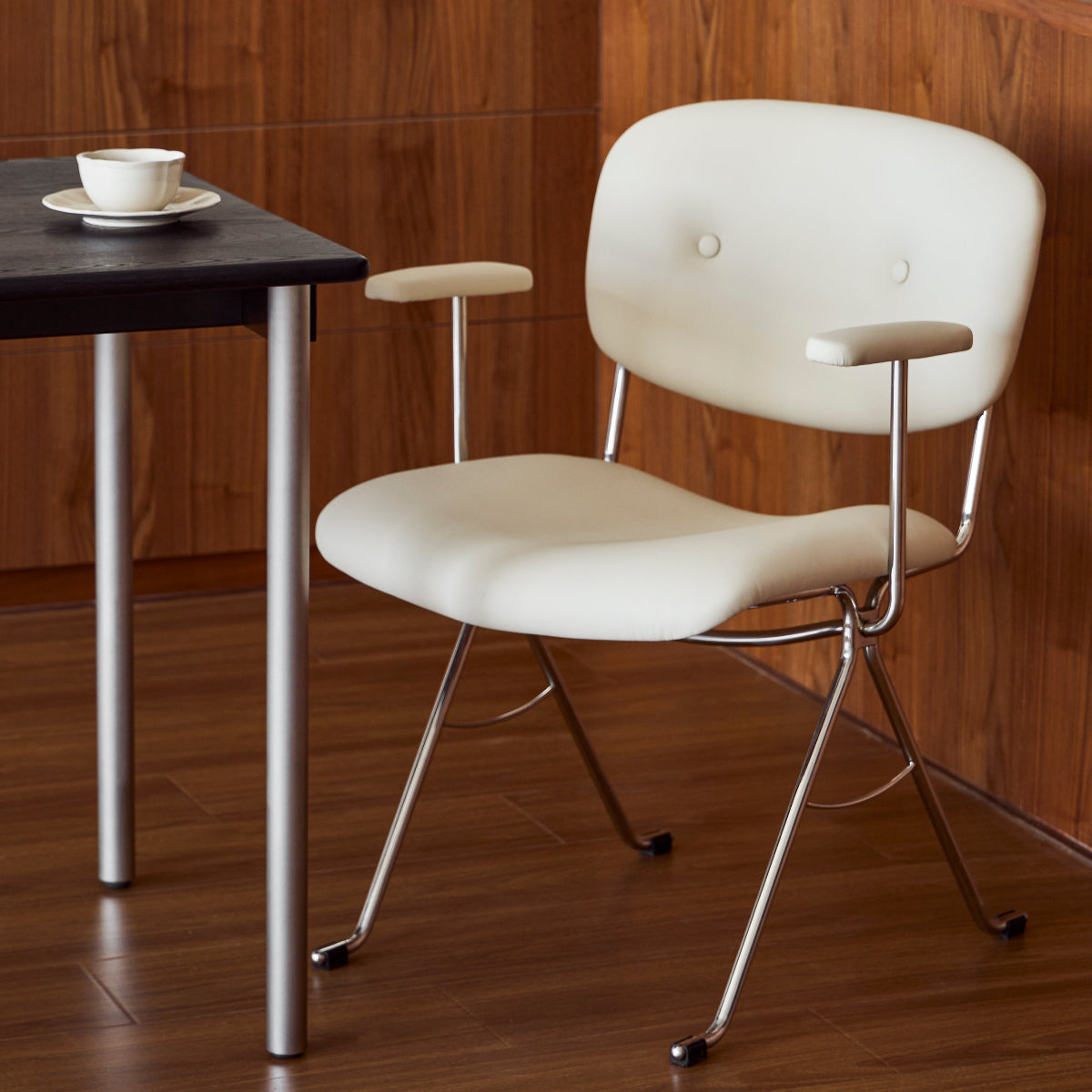 White chair with metal legs next to a black table in a room with wooden walls.