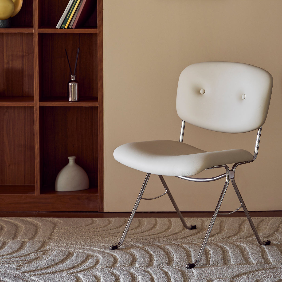 White chair in a room with a wooden bookshelf and framed picture on the wall.