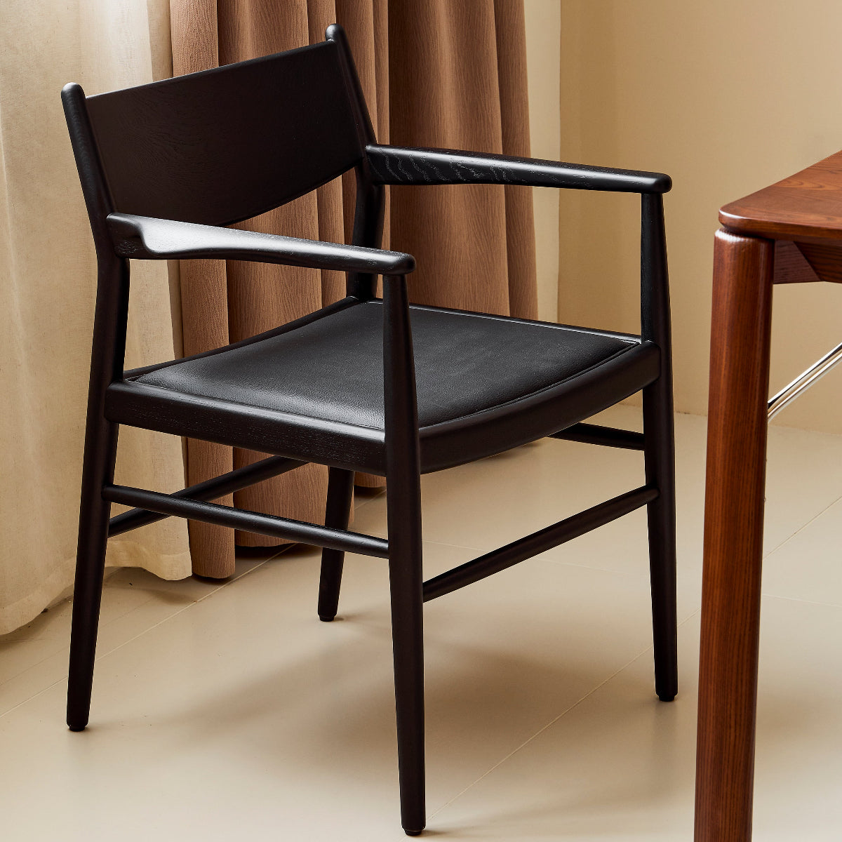 Black chair with a wooden table against a beige curtain background