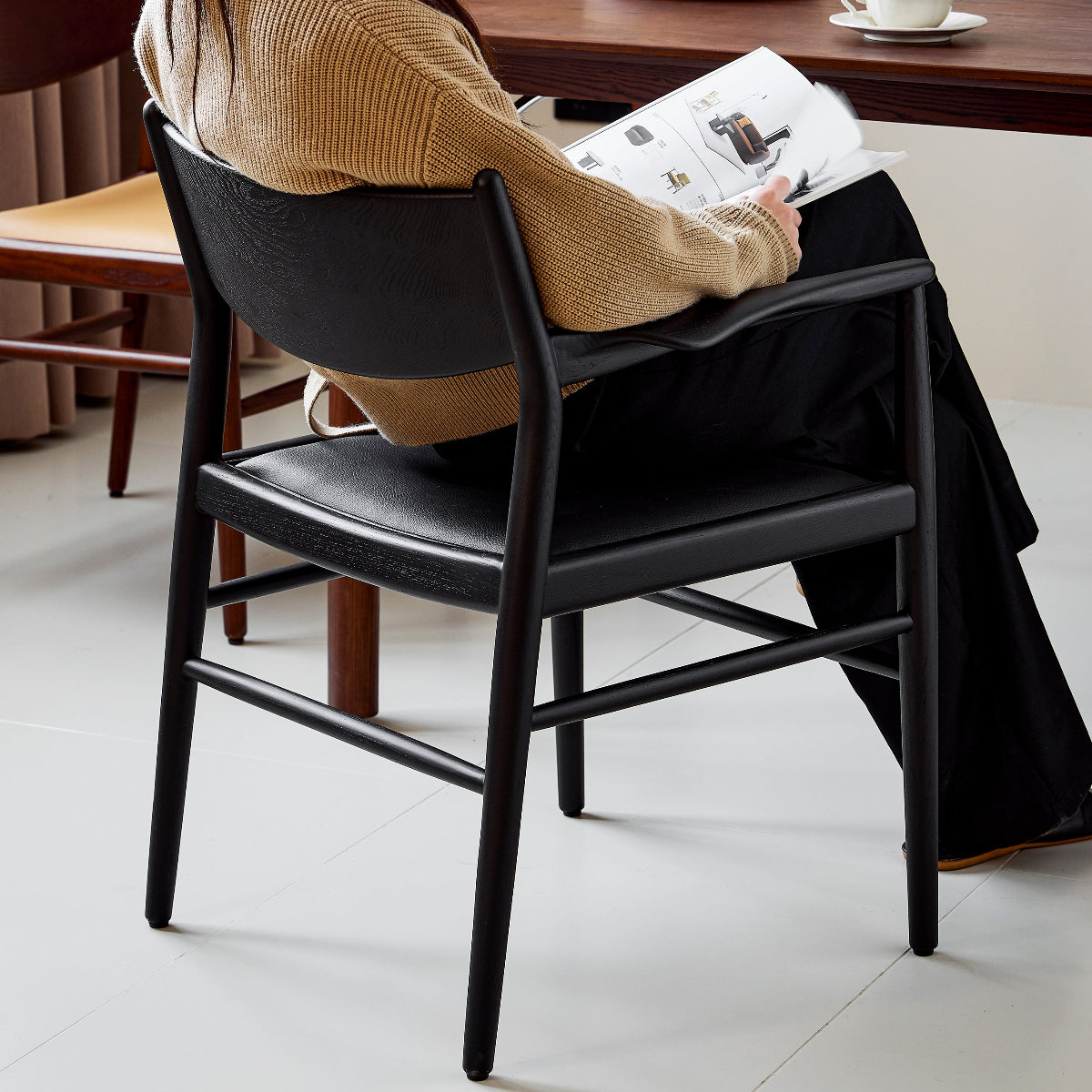 Person sitting at a table with a plate of food and a cup, reading a newspaper.