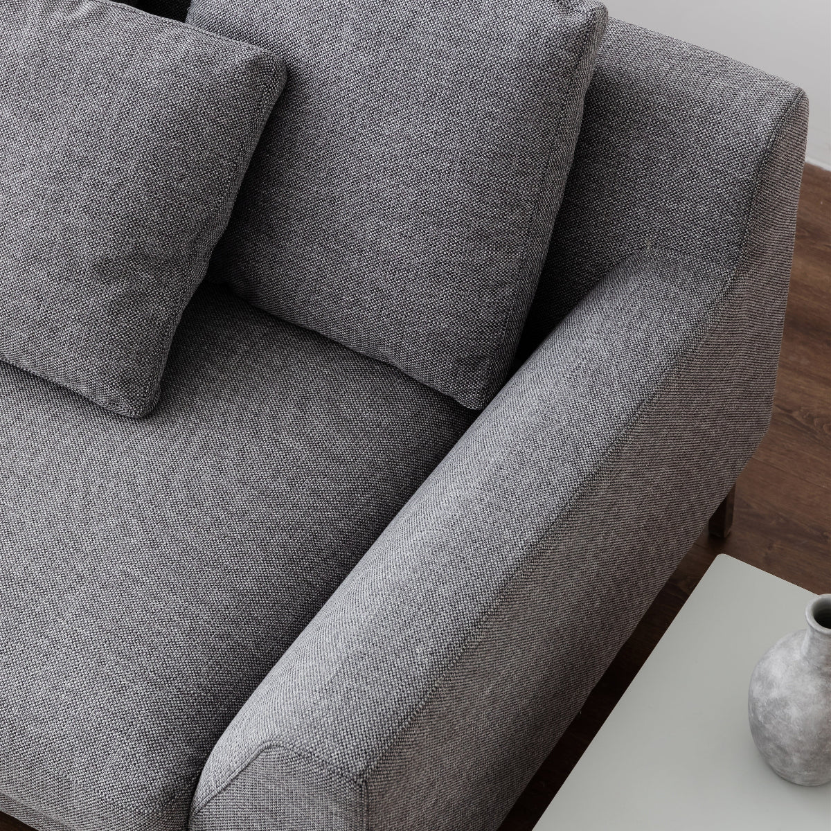 Gray sofa in a room with a white side table and decorative vase.