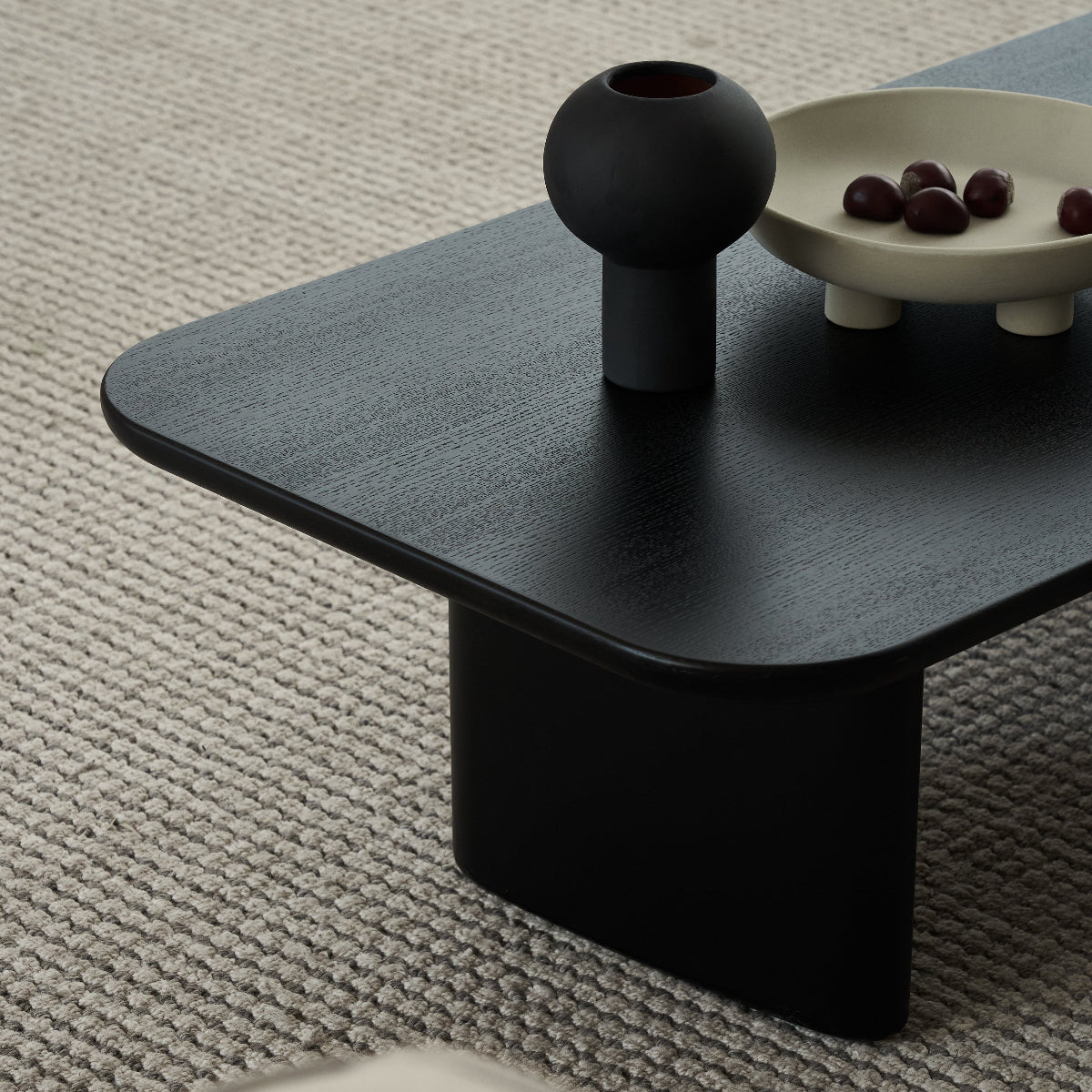Black coffee table with a vase and bowl on a textured gray floor
