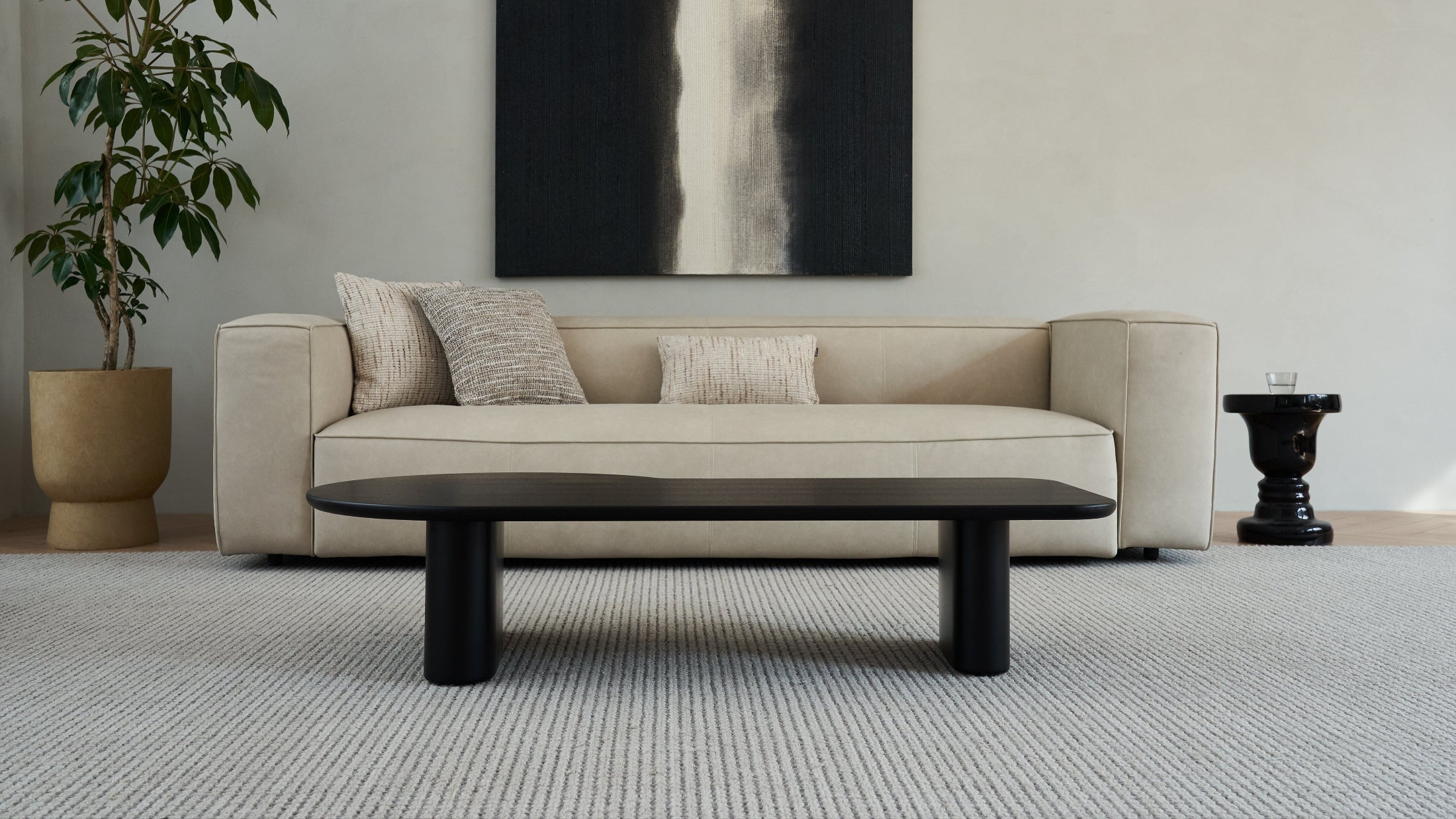 Beige sofa with black legs in a room with a plant and abstract art on the wall.
