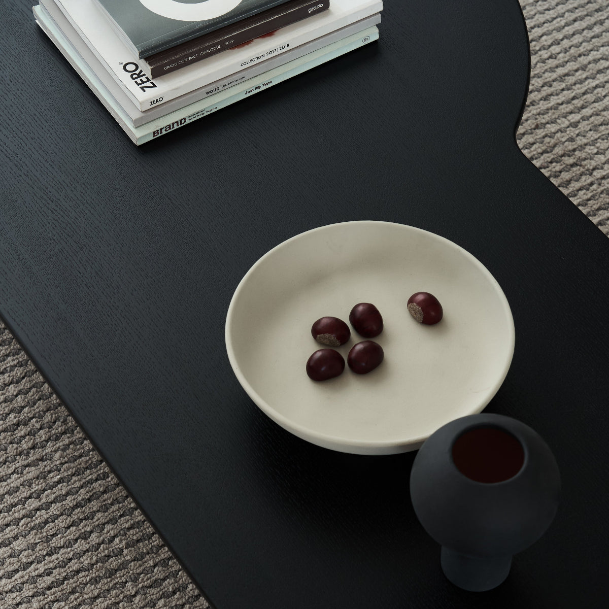 White bowl with cherries on a black surface next to a gray textured rug