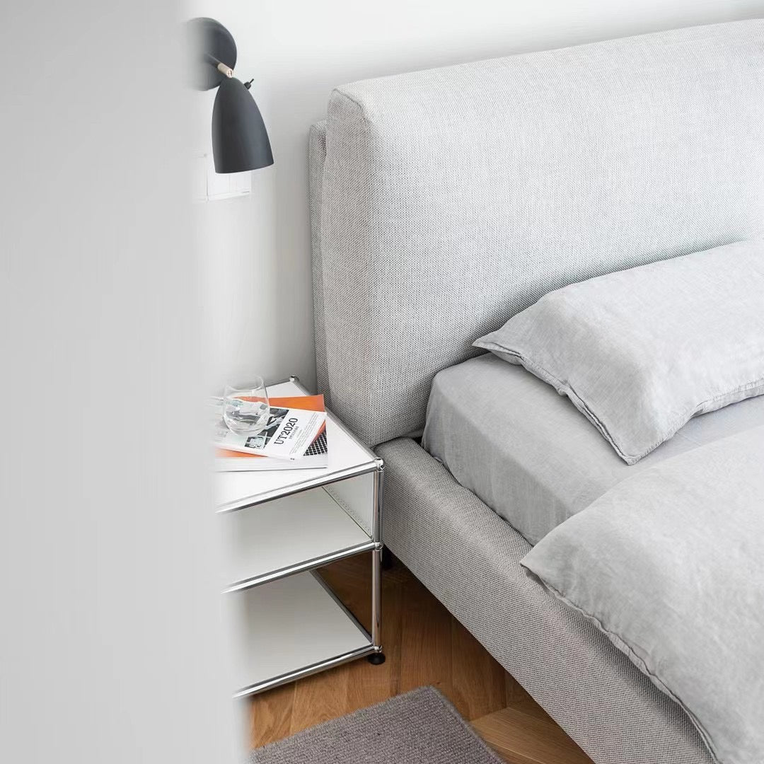 Gray bedroom with bed, nightstand, and slippers on a rug.