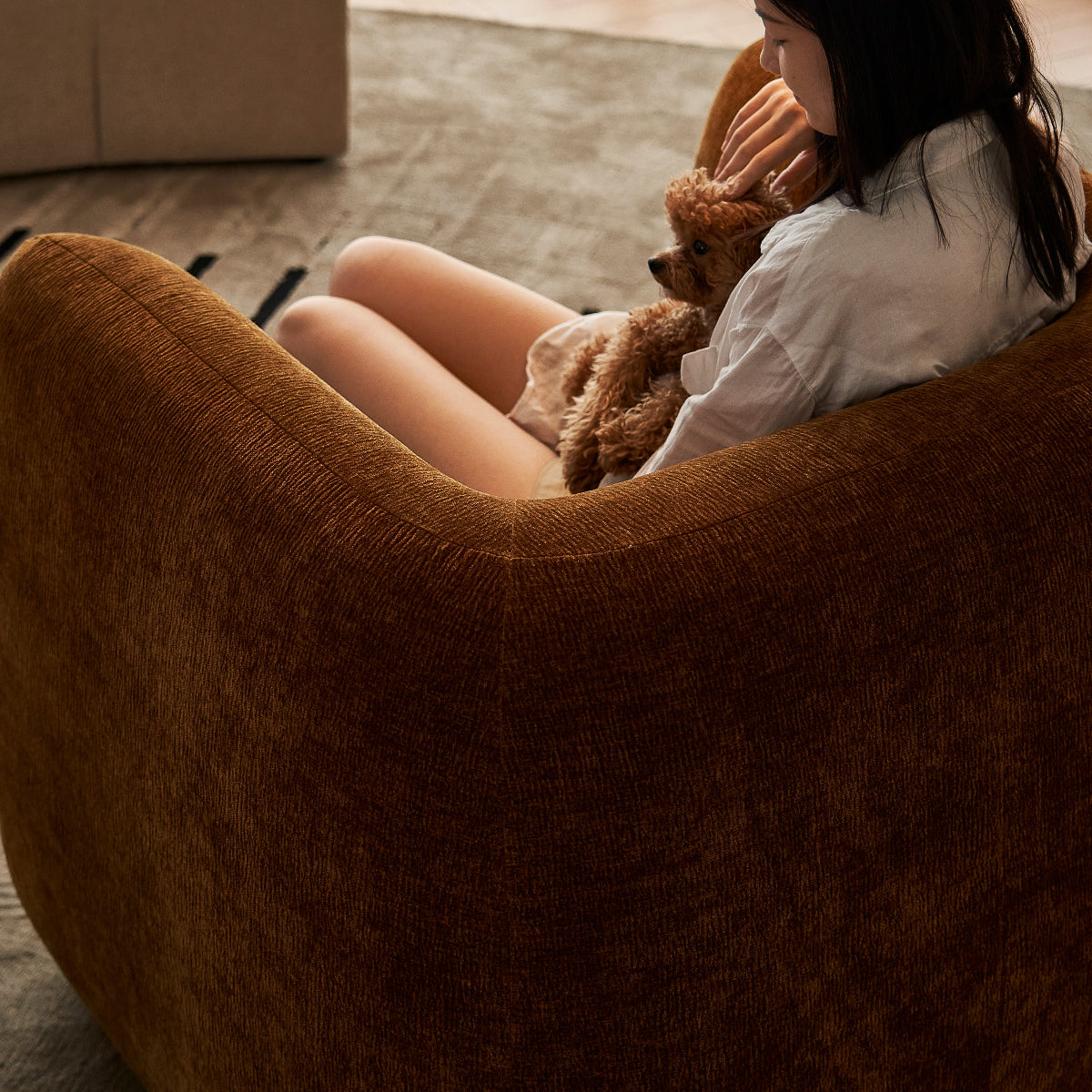 Woman sitting on a brown chair holding a teddy bear in a cozy living room.