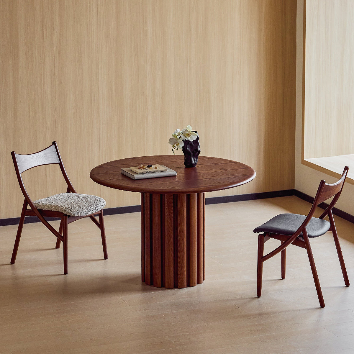 Round wooden table with two chairs in a room with striped wallpaper.
