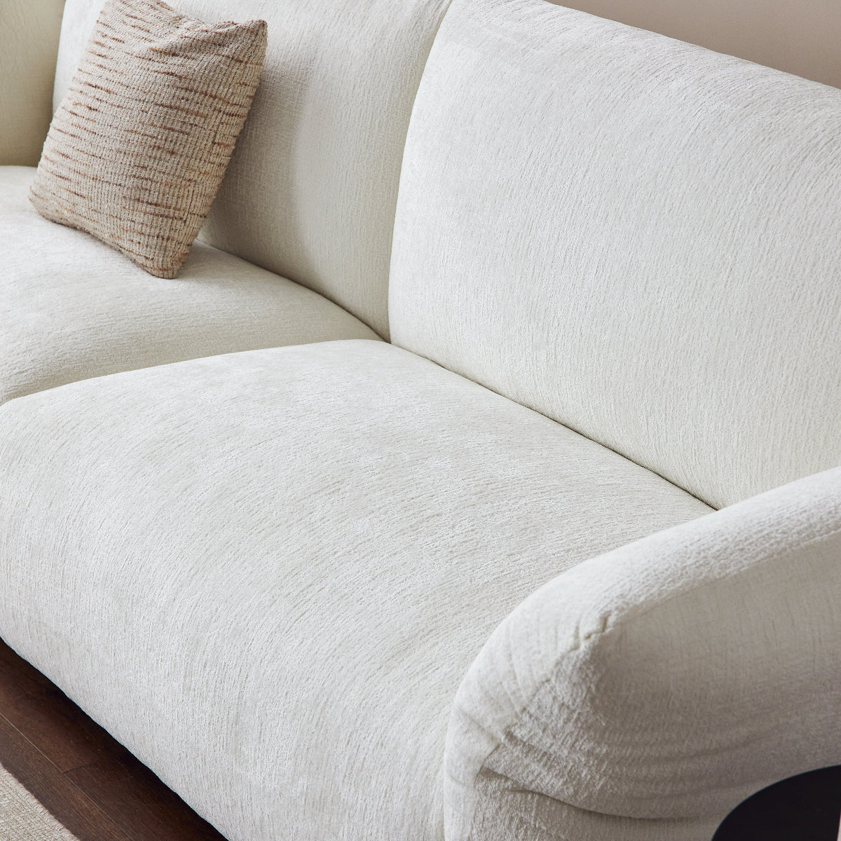 White sofa with a textured pillow against a beige wall