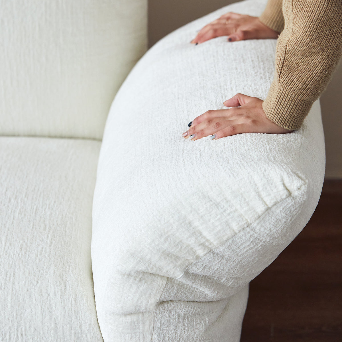 Person wearing white pants and a beige sweater sitting on a white couch.