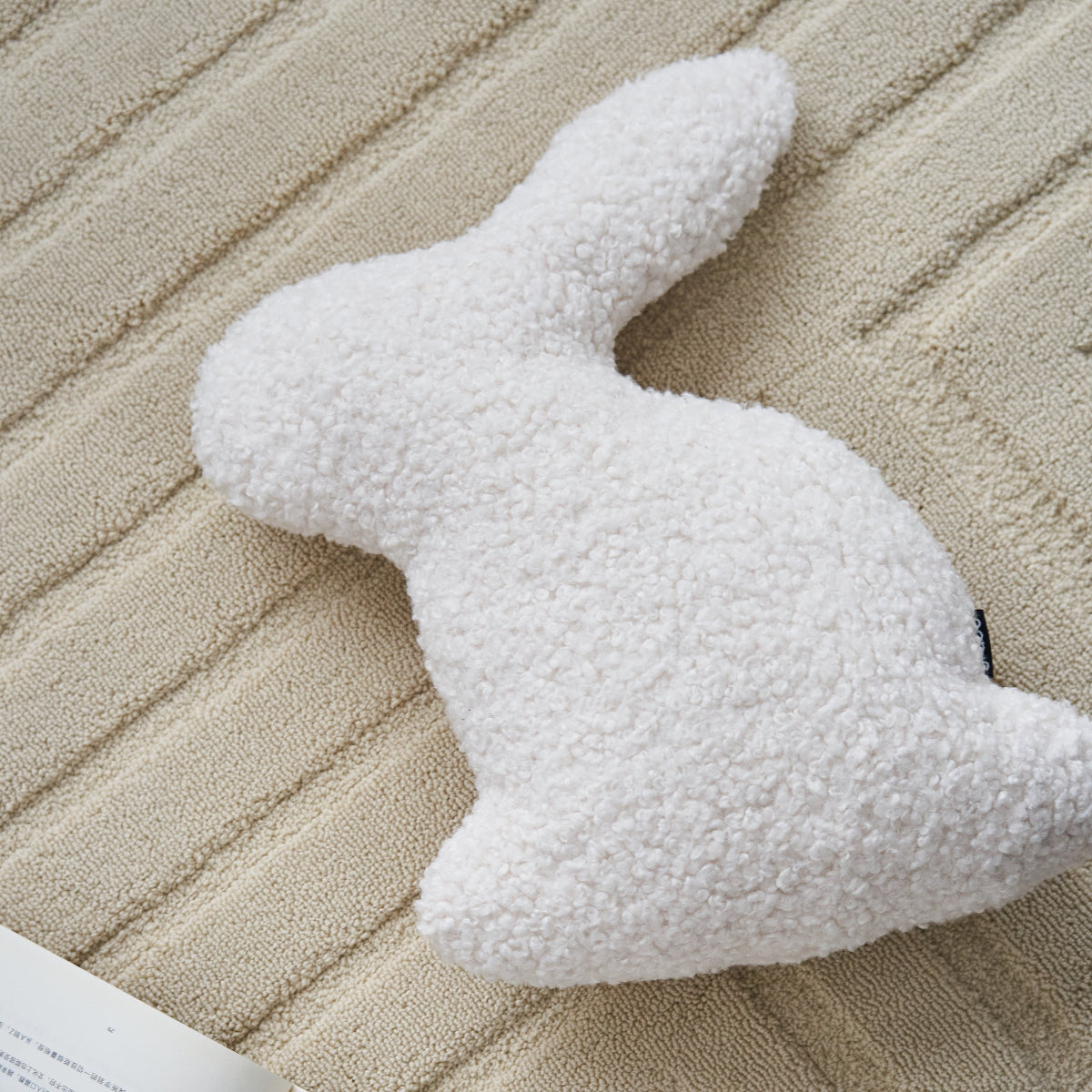 White plush swan toy on a textured beige surface with an open book and a cup nearby.