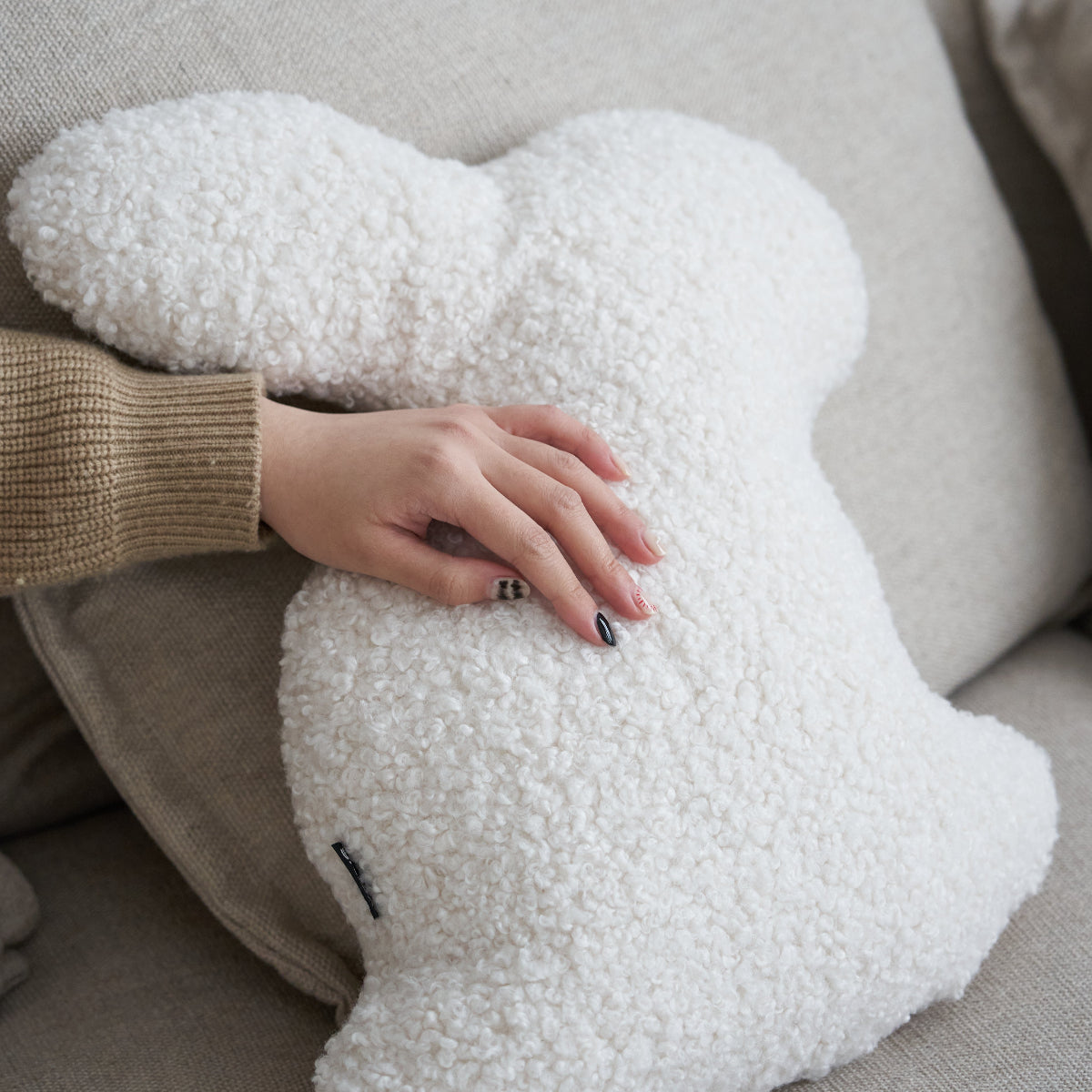 White fluffy pillow held by a person on a beige couch