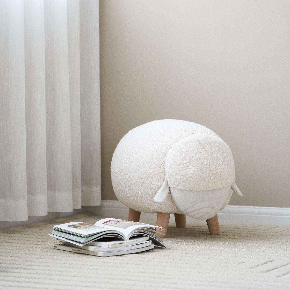 Round white ottoman with wooden legs on a light wooden floor next to a window with blinds.