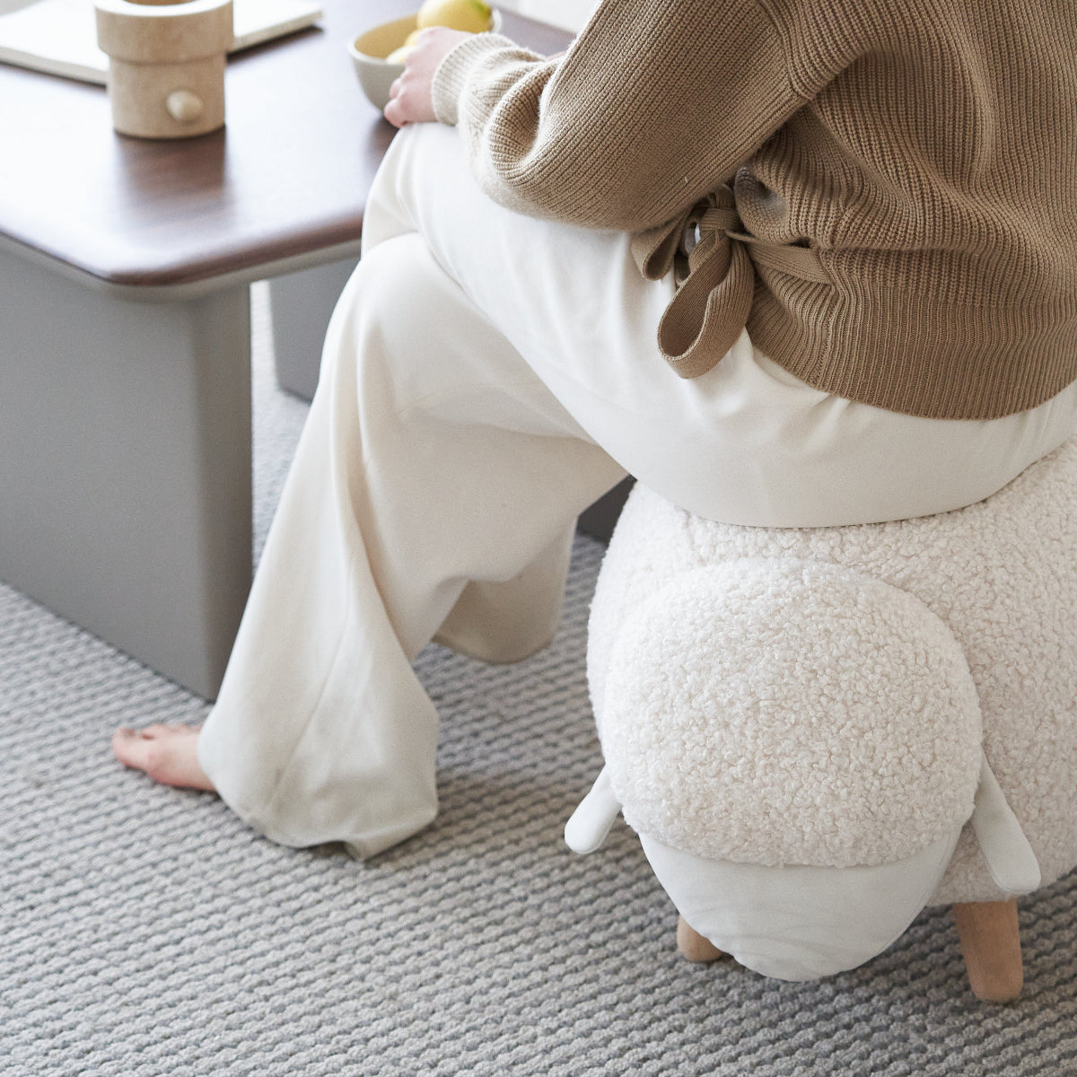 Person sitting on a fluffy white animal-shaped stool in a cozy living room.