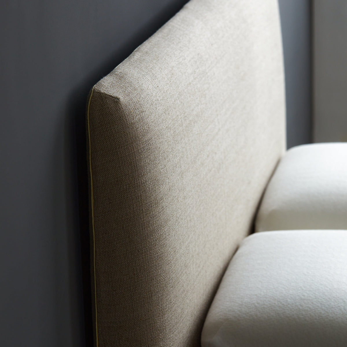 Close-up of a beige upholstered headboard against a dark wall.
