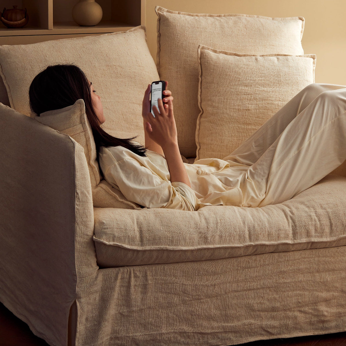 Person lying on a beige sofa using a smartphone in a cozy living room.