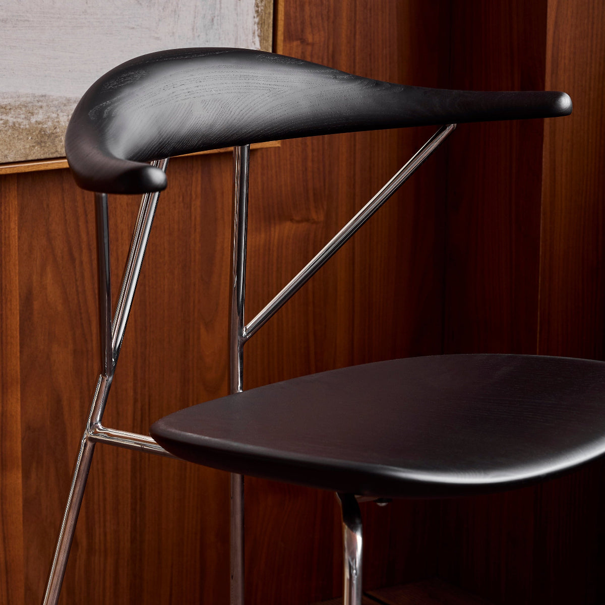 Black chair with metal legs against a wooden wall.