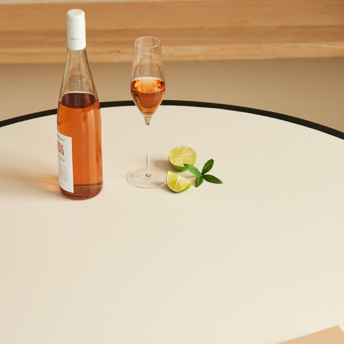 Bottle of rose wine, glass with rose wine, lemon slices, and a book on a round table.