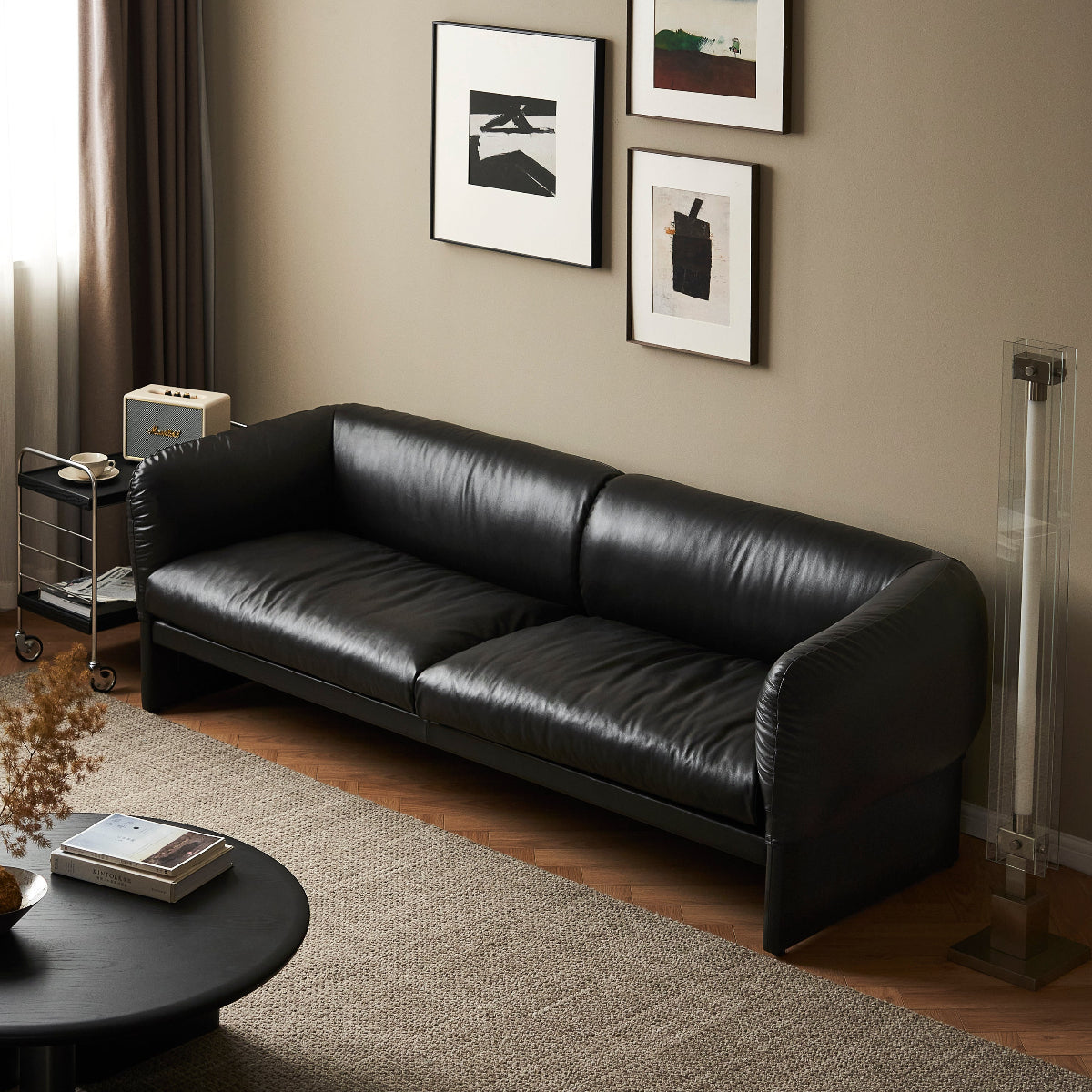Modern living room with a black leather sofa and framed pictures on the wall.