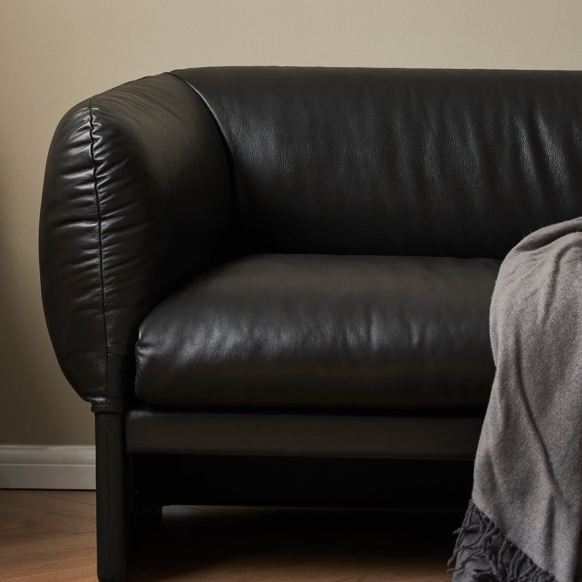 Black leather sofa with a gray blanket on a beige wall background