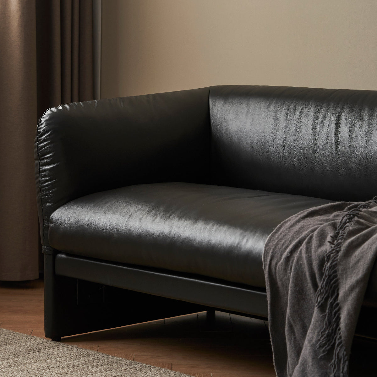 Black leather sofa with a gray throw blanket in a room with beige walls and a textured rug.