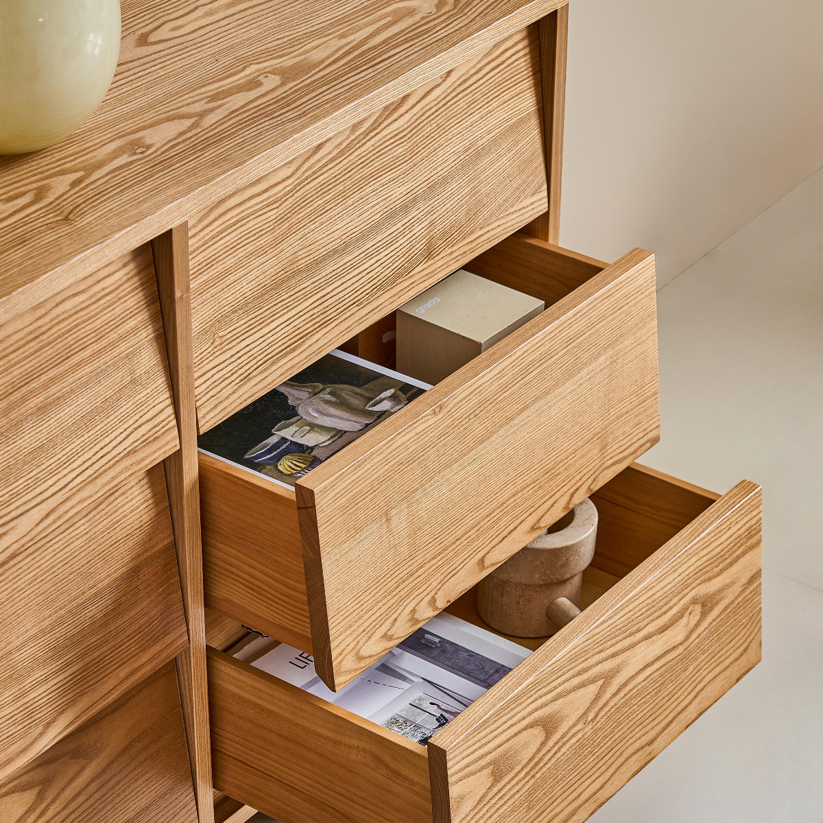 Wooden dresser with open drawers containing magazines, on a light-colored floor.