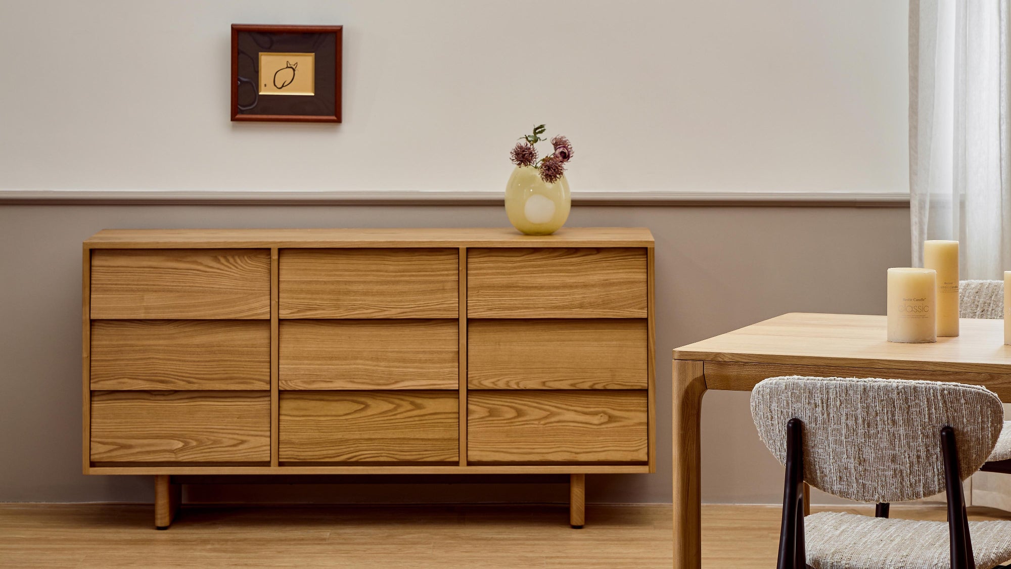 Wooden dresser with a vase of flowers next to a dining table with chairs in a room.