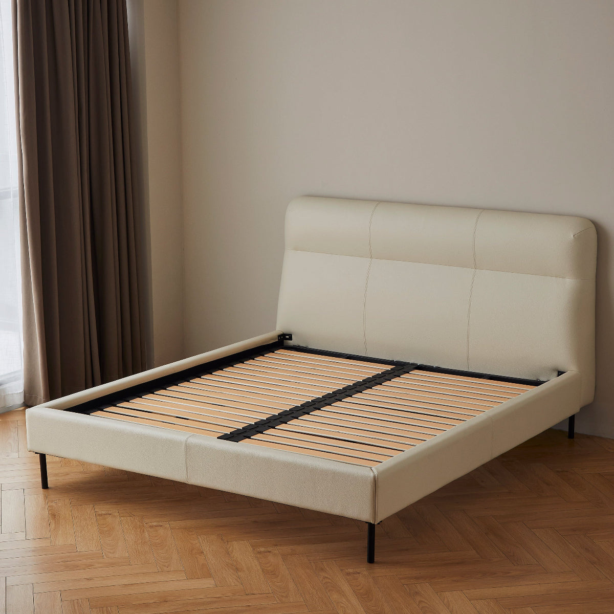 Beige upholstered bed frame in a room with beige walls and wooden flooring.