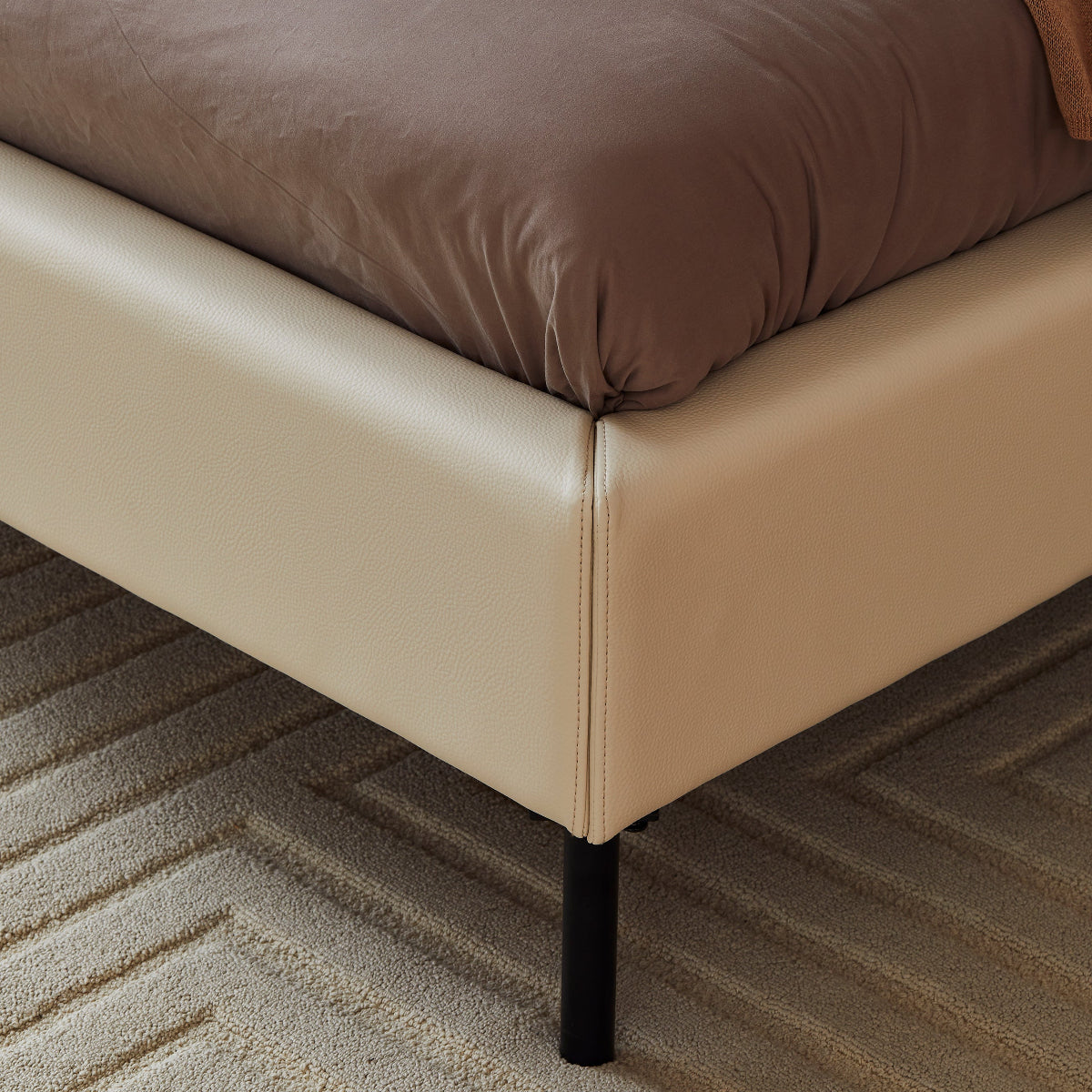 Beige bed frame with a brown mattress on a carpeted floor