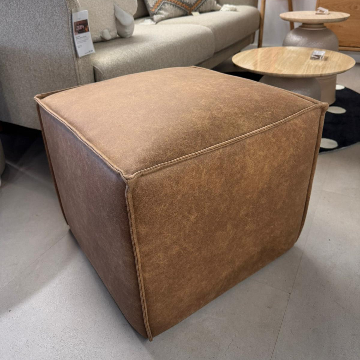 Brown ottoman in a living room setting with a sofa and coffee table.
