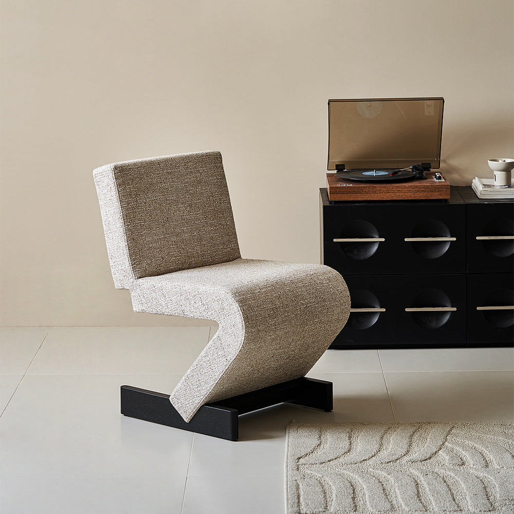 Modern chair in a room with a black cabinet and framed artwork on the wall.