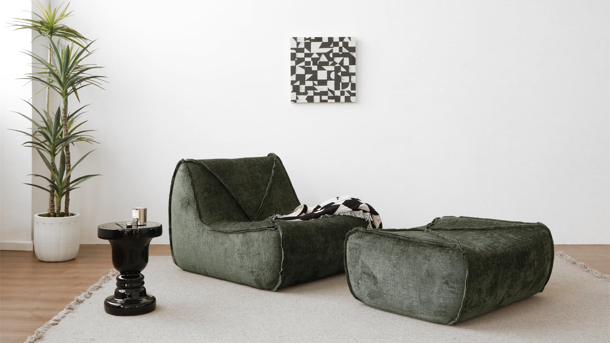 Green sofa and ottoman in a minimalistic living room with a plant and wall art.