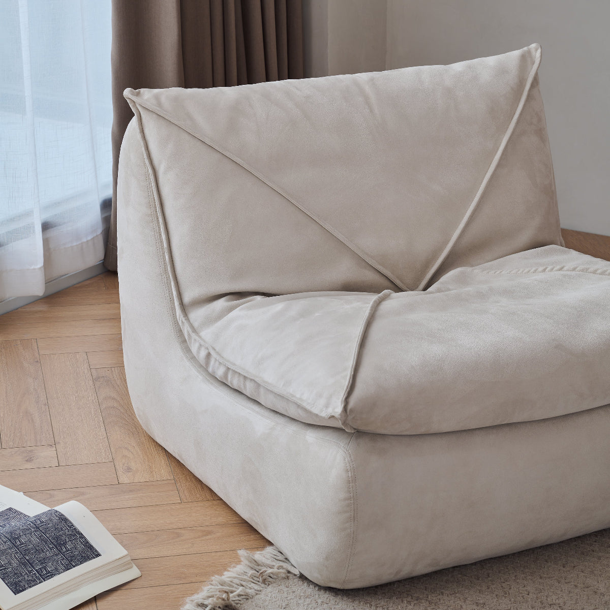 Beige bean bag chair on a wooden floor with a curtain in the background