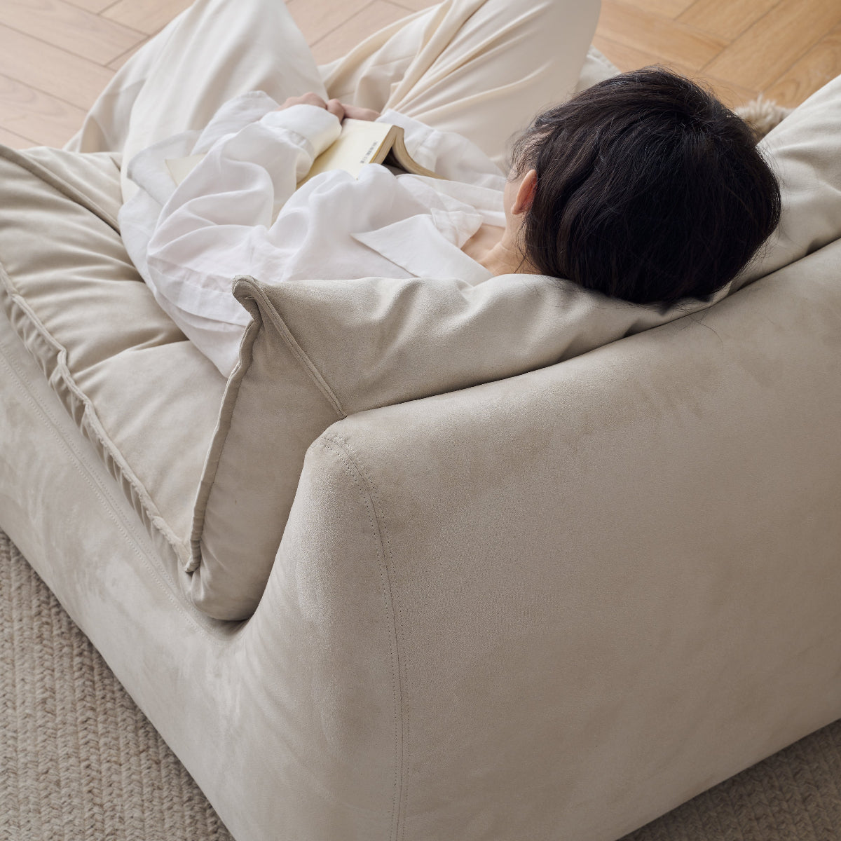 Person lying on a beige sofa in a room with wooden flooring.