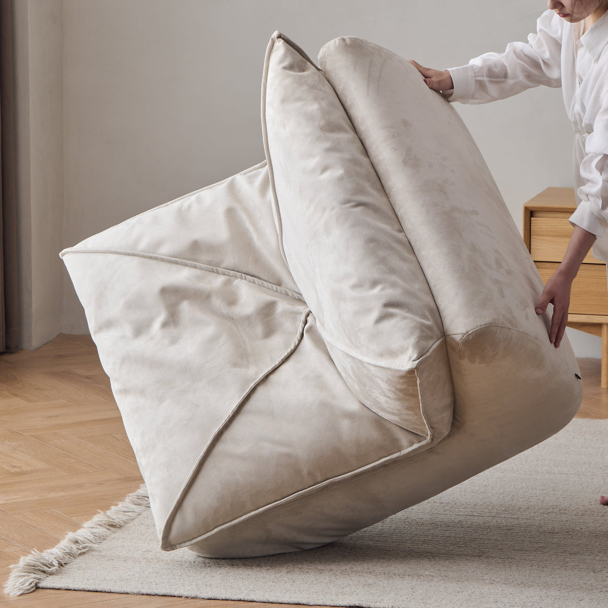 Person adjusting a large beige cushion in a minimalistic room.