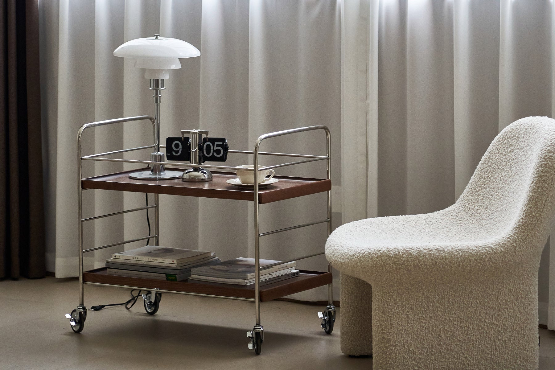 Cart with books and a lamp next to a textured chair against a curtain backdrop