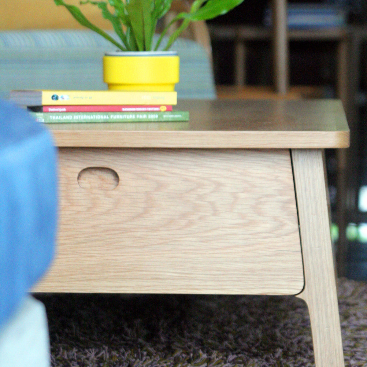 Wooden side table with books and a plant in a yellow pot on top, blurred background